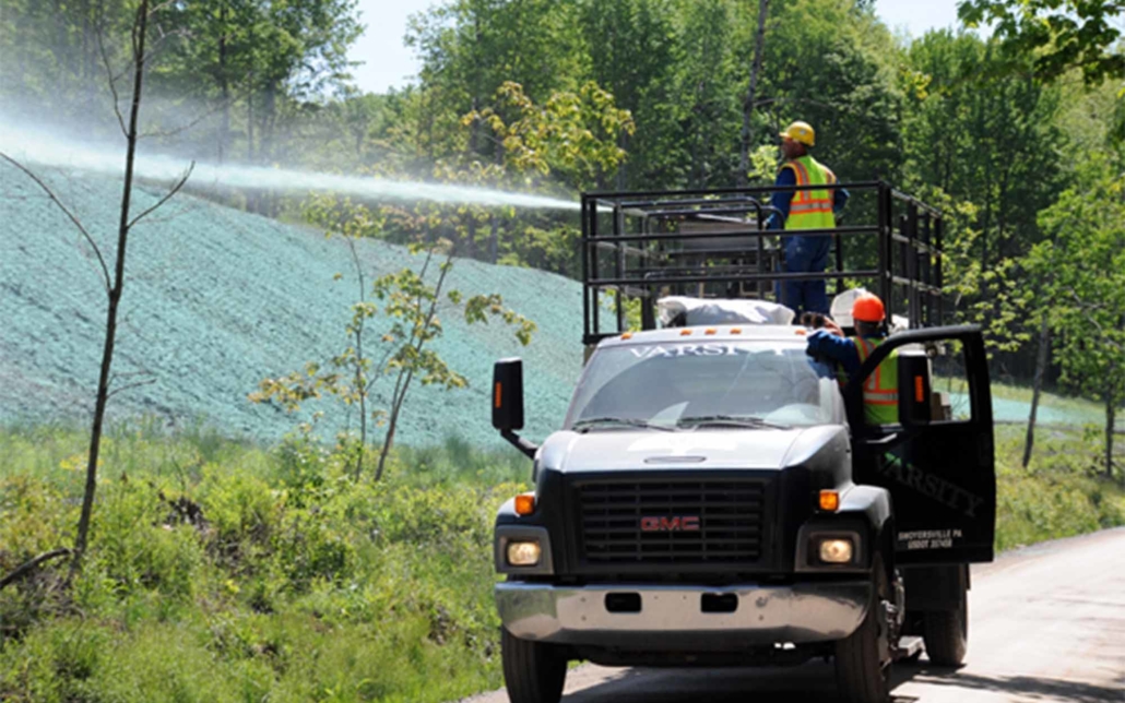 Varsity crew on a truck spraying a material on a hilll